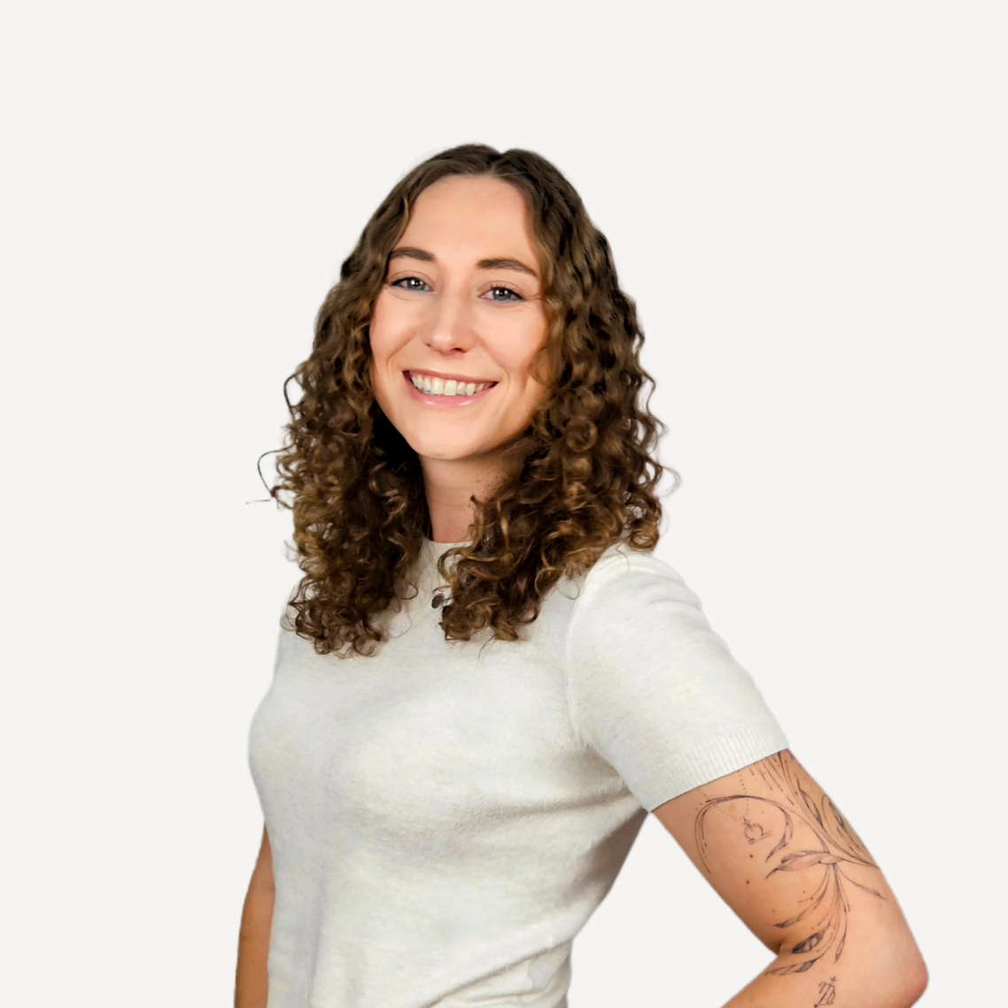 Portrait 2 Hannah Sophie Welte Lächelnde Frau mit lockigem Haar, trägt ein helles T-Shirt und hat ein Tattoo am Arm.